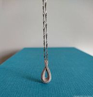 Clear image showing the pendant hanging from the chain against a blue background, highlighting the sparkling stones and teardrop shape.