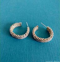 Photo showing two sterling silver woven hoop earrings laying flat on a blue surface, showing front side and weave detail.
