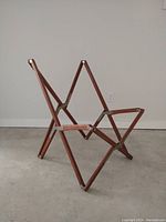 Side view of vintage folding teak chair frame showing steel hinges and X-frame structure.