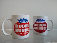 Two vintage white ceramic coffee mugs with red and blue Fleer Dubble Bubble logos on each side, front view.
