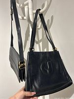 Two black leather handbags hanging on a white coat rack, showing logos and shape of bags.