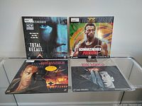 Four LaserDiscs displayed on a glass shelf showing front cover art for Total Recall, Predator, Die Hard, and Die Hard 2.