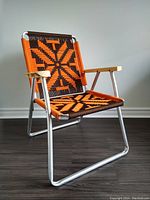 Front angled view of the vintage lawn chair showing the custom orange and brown woven seat and aluminum frame with wooden armrests.