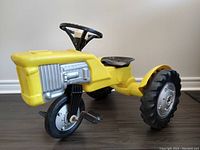 Front side angled view of the yellow pedestal tractor showing the silver engine detail and metal pedals.