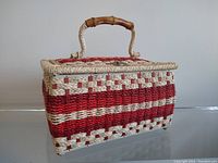 Side angle view of woven sewing basket showing red and natural color weave, bamboo handle, and basket shape.