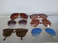 Six pairs of vintage sunglasses displayed on a glass surface showing various lens colors and frame styles.