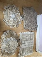 Top view of several crochet and lace doilies and table runners in neutral colors laid on wooden floor
