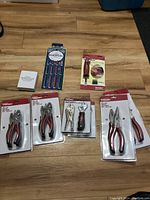 Assortment of hand tool sets on wooden floor showing packaging for several plier sets, mini wrench set, Robertson bit sets.