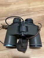 Top view of binoculars showing central focus wheel, textured body, and leather strap detail.