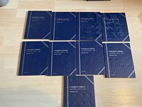 A top-down view of 9 blue binders labeled 'Canadian Nickels Collection 1922 to 1960 Number One' laid out on a wood floor, showing the front covers.