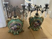 Photo of matching pair of vintage porcelain candle holders with metal candelabra arms and floral painting.