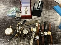 Photo of eleven watches including ten wristwatches and one pocket watch, some in case boxes and a small decorative heart-shaped trinket box.