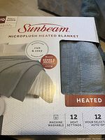 Photo of new in box Sunbeam queen size microplush heated electric blanket packaging showing product features including 12 heat settings, 12 hour auto-off, machine washable.