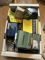 Box filled with various fishing reels, lures, and accessories including Panther Martin spinner lures in yellow package, Alvey fishing reel boxes, and a Penn box.