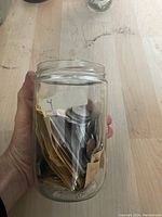 Hand holding a glass jar filled with mixed coins and paper envelopes