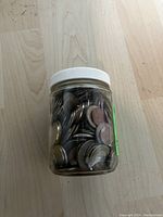 Clear glass jar with white lid filled with worn foreign coins.