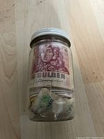 Glass jar filled with folded and rolled foreign currency notes dominated by a Dutch Gulden note with a portrait.