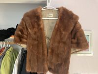 Brown fur shawl hanging on hanger showing short sleeves and beige lining label inside