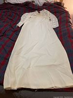 Full length view of white wedding dress showing lace bodice and sleeves, with plain long skirt laid on bed