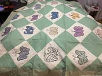 Photo shows the full queen size handmade quilt spread on a bed. The quilt features a green and white large check pattern with colorful butterfly appliqués on the white squares.