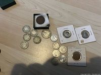 Overview of lot showing multiple coins spread out on table, including 1920 penny in green box and several quarters and nickels.