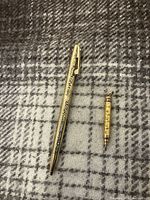 Photo showing gold tone pen and mechanical pencil on a gray plaid fabric background.
