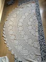 Photo showing detailed crochet lacework of round tablecloth laid partially on a patterned rug on wooden floor.