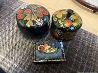 Three Russian laquer boxes: two round with floral and fruit motifs, one rectangular with folk art scene