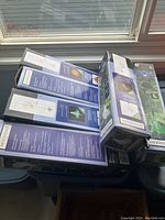 Stack of six Moonrays solar garden light boxes piled on a surface by a window, showing product packaging and partially visible design and branding.