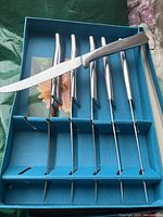 Set of six new serrated steak knives in silver handles neatly arranged in original blue box with floral interior