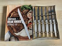 Top view of box and 6 steak knives in a gold-colored tray, box labeled with '6 Pieces Couteaux Steak Knives Mundial' and showing steak and vegetables image.