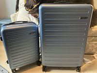Photo of two blue hard plastic suitcases with horizontal ridges and four wheels each, one large and one smaller, both in good condition.