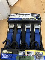 Photo showing four blue cam buckle tie down ratchet straps in original box with packaging information.