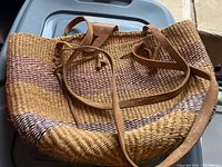Photo of woven hand bag showing natural and colored fibers with leather straps laid out.