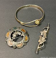 Photo showing all three jewelry pieces: one bangle and two brooches, laid flat on table.