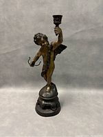 Front view of 1950s bronze cherub statue candleholder holding one candleholder and bow standing on a decorated oval base