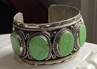 Front angled view of the sterling silver cuff bangle showing four oval lime green turquoise stones with silver rope and bas-relief detailing.