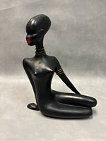 Side view of the seated West German Nubian figurine showing smooth black finish, gold-tone neck and arm rings, and detailed facial features.
