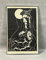 Framed erotic woodblock print showing stylized nude female figure against full moon, black and white, in metal frame