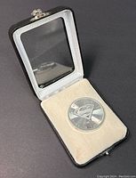 Silver coin featuring Superman logo displayed inside black and white fitted presentation box with transparent lid showing the coin.