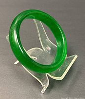 Front angle view of the green jade bangle on a clear display stand showing its round shape and rich green color.