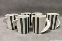 Front view of all six coffee mugs showing striped pattern and dome handles arranged in an arc.