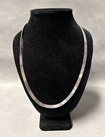 Full front photo of the 24 inch long flat silver chain necklace displayed on a black mannequin stand.
