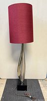 Full view of the tall lamp showing its burgundy fabric shade and aluminium body with black square base.