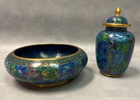 Footed bowl and covered jar displayed side-by-side showing enamel floral patterns and gold-tone trim.