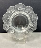 Front view of glass bowl showing frosted leaf motif around rim and clear central basin, placed on stand against dark background.