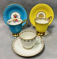 Front view of three demitasse teacups and matching saucers showing color and decorative details