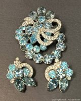 Front view of the brooch and earrings showing blue crystals and rhinestones on black background