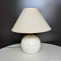 White ceramic ball lamp with original light fabric shade that shows discoloration. Lamp base is glossy and smooth.