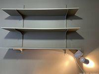 Three wall shelves installed on grey vertical metal tracks, painted grey shelves with white brackets. Shelves are adjustable and appear lightly used with some wear.